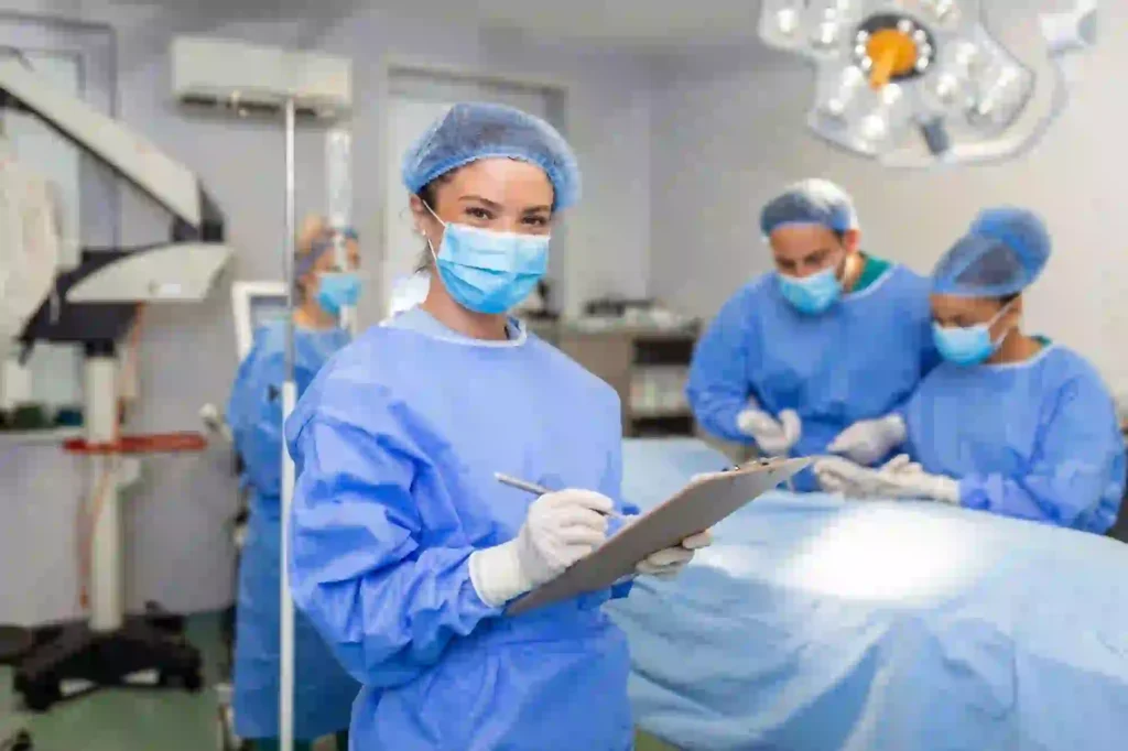 Doctor in blue surgical scrubs with a mask and clipboard inside an operation theatre during a C-section procedure.