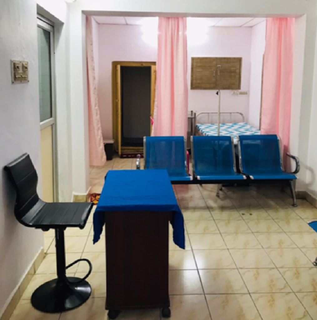 Interior view of a women's clinic OPD in Avadi with seating area, consultation table, and inpatient bed separated by curtains.